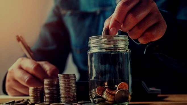 A hand dropping a coin into a savings jar